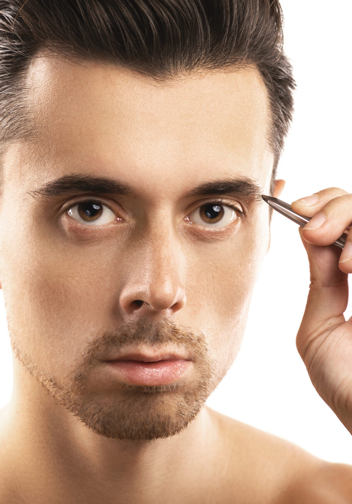 Beauty for men. Young guy holding tweezers near his eyebrow for that's shape correction.